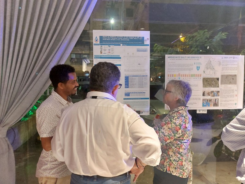 Three Hub members smile and discuss the poster displayed on a glass wall